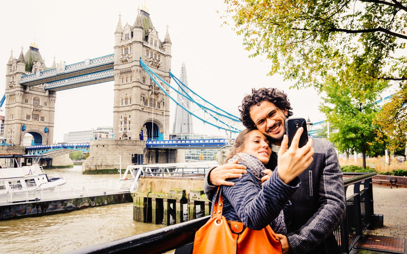 Et par holder rundt hverandre mens de tar selfie foran en bro
