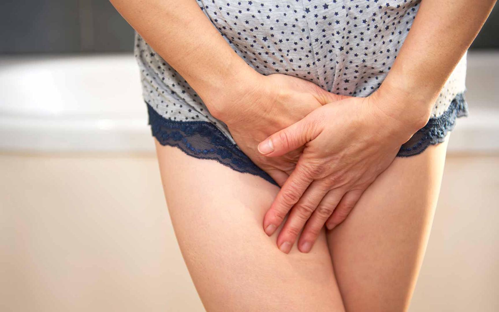 Bilde av underkroppen til en kvinne som står på et baderom. Hun er iført undertøy og holder hendene i kryss foran underlivet.