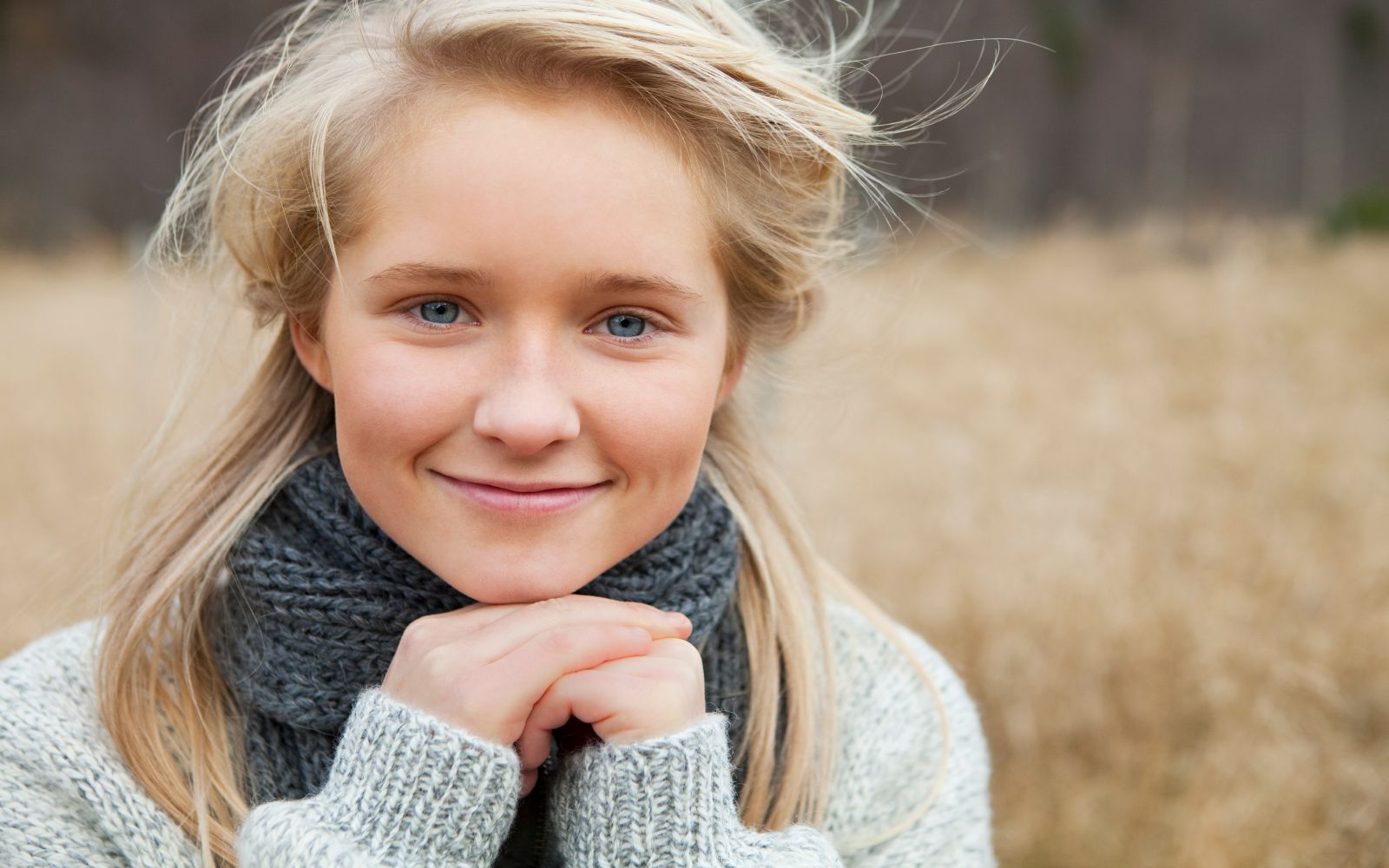 Kvinne med blondt hår og blå øyen med strikket genser og skjerf