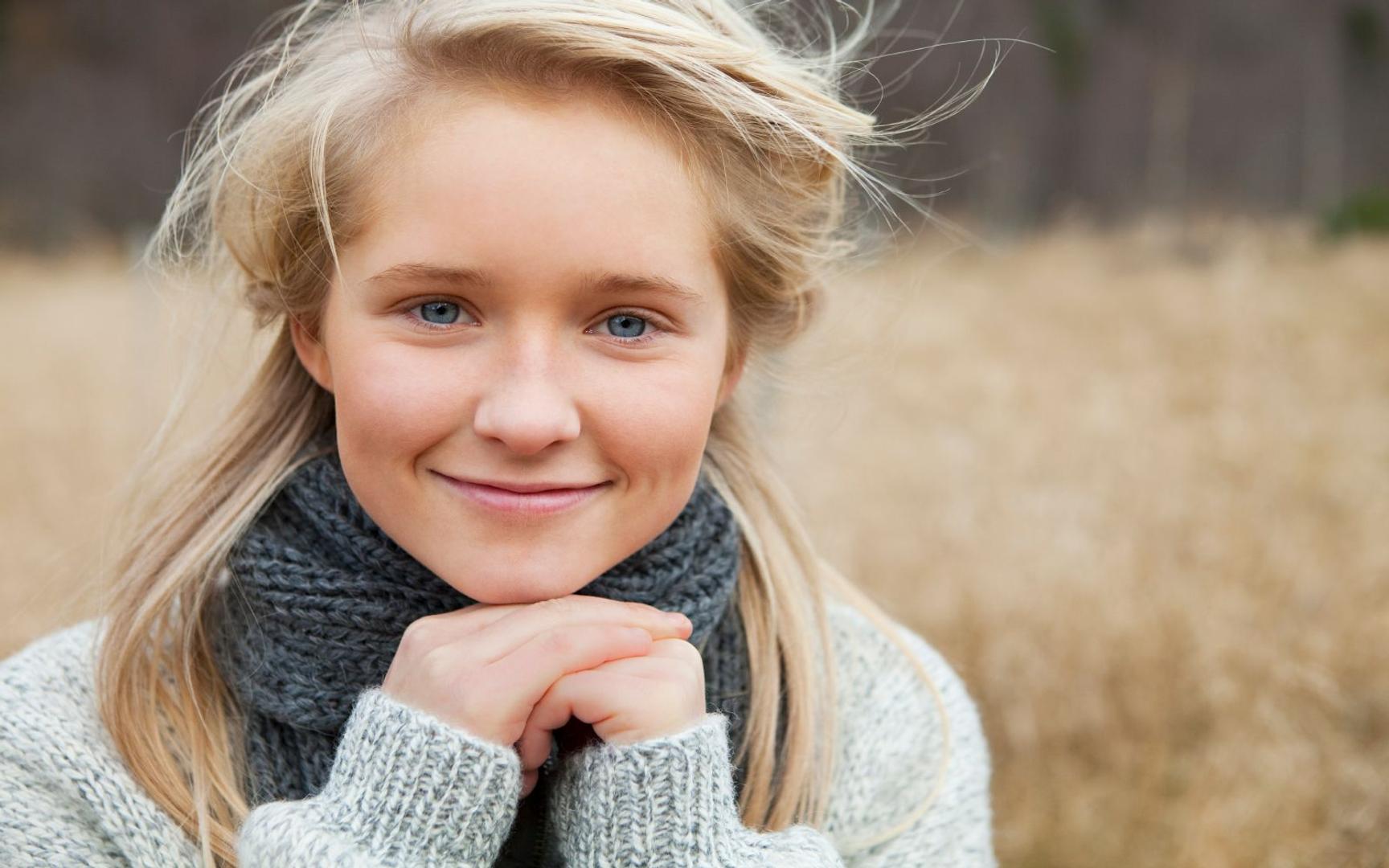 Kvinne med blondt hår og blå øyen med strikket genser og skjerf