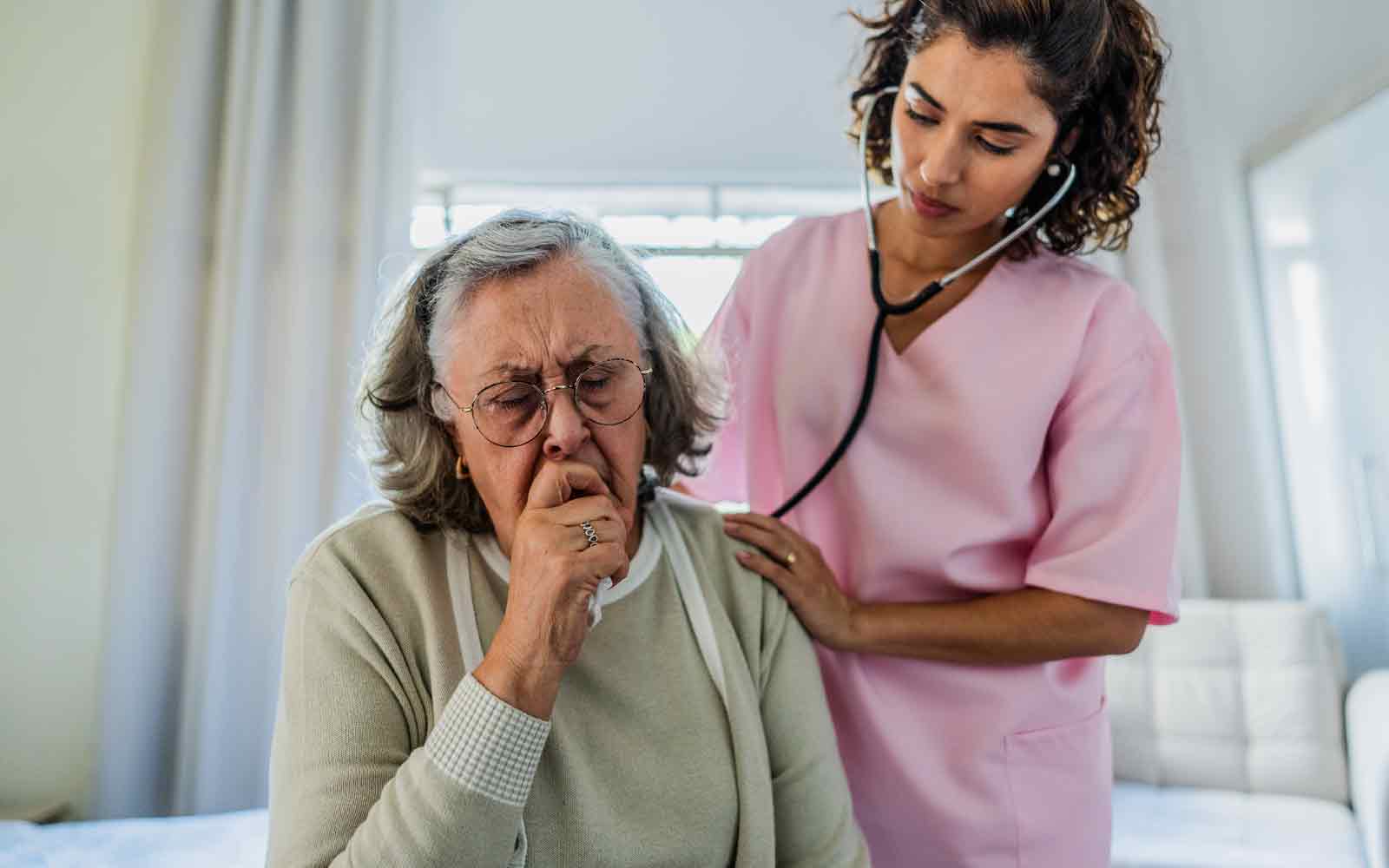 Sykepleier lytter på lungene til hostende, eldre kvinne
