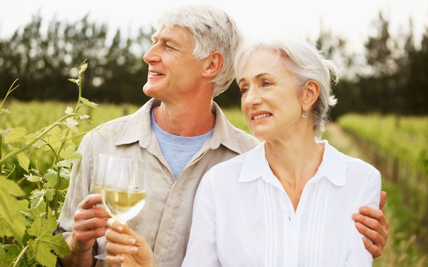 Eldre par nyter hvitvin i vingård.