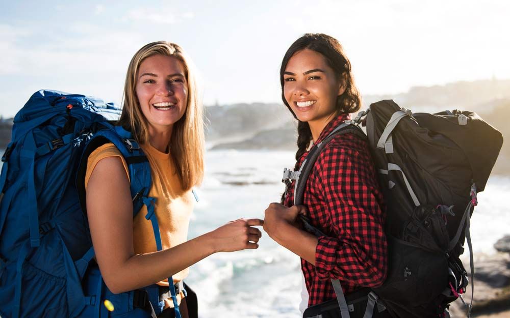 To kvinner på tur med ryggsekker smiler mot kameraet