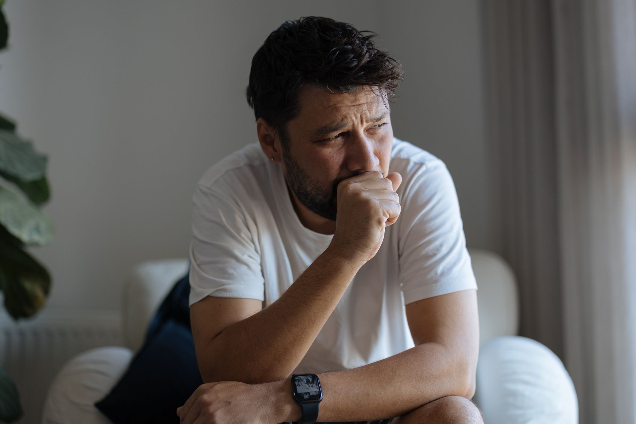 En mann sitter fremoverlent og hoster inn i hånden