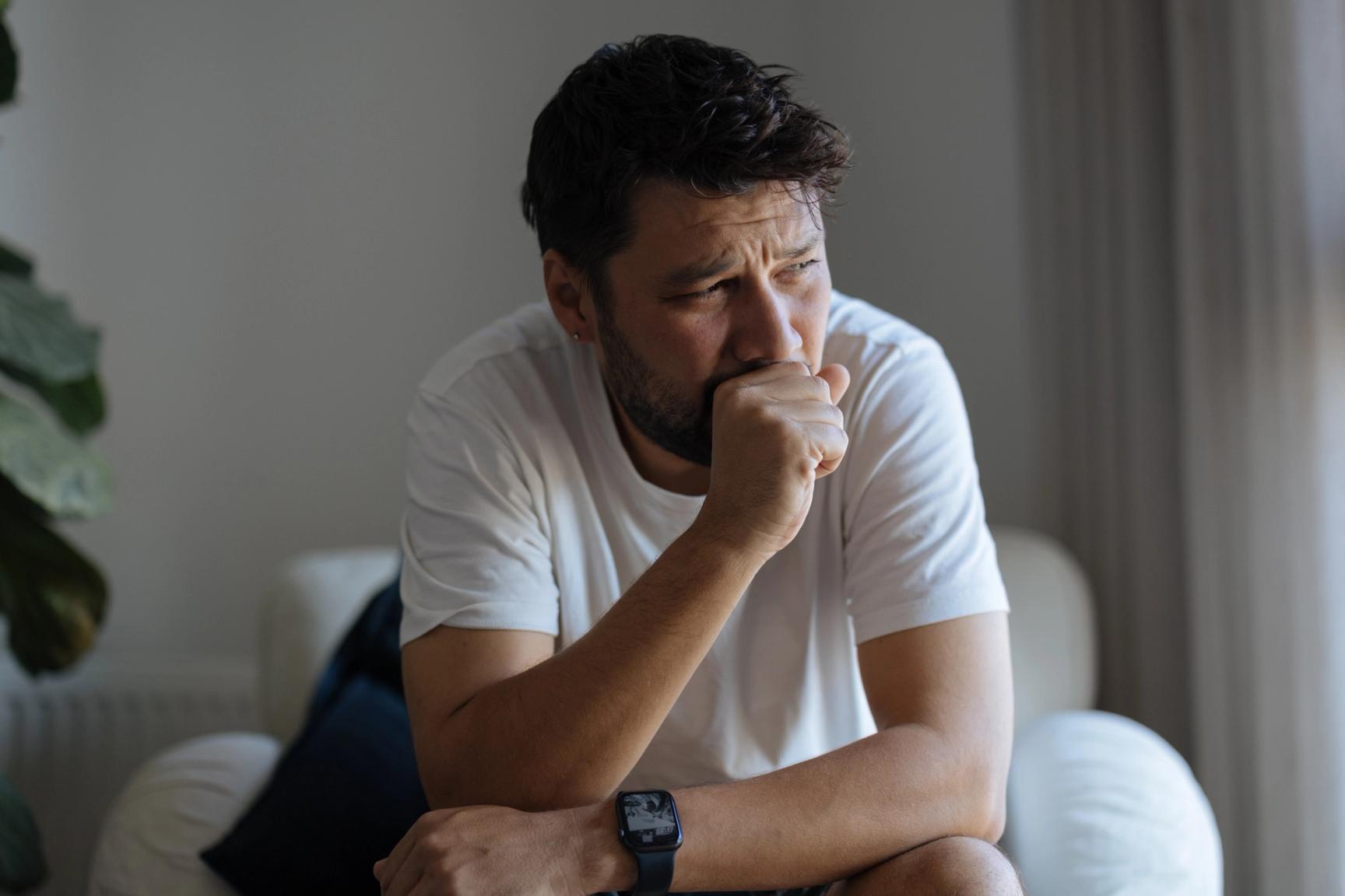 En mann sitter fremoverlent og hoster inn i hånden