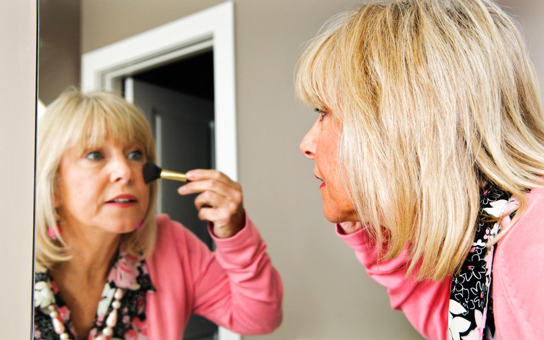 Kvinne foran speilet påfører sminke
