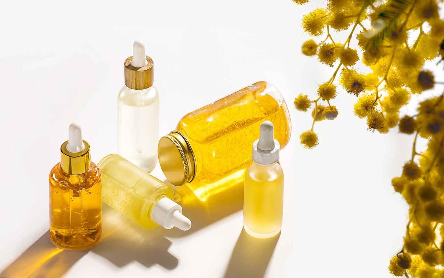 4 pipetteflasker med hudpleieoljer i ulike gule nyanser på hvit bakgrunn. Vitamin E er fettløselig og godt egnet til hudpleieformuleringer som olje og krem.