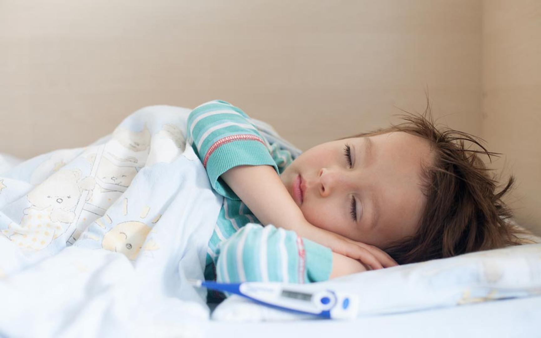 Bilde av et barn som sover i en seng med hendene under hodet og en febermåler ved siden av puten.