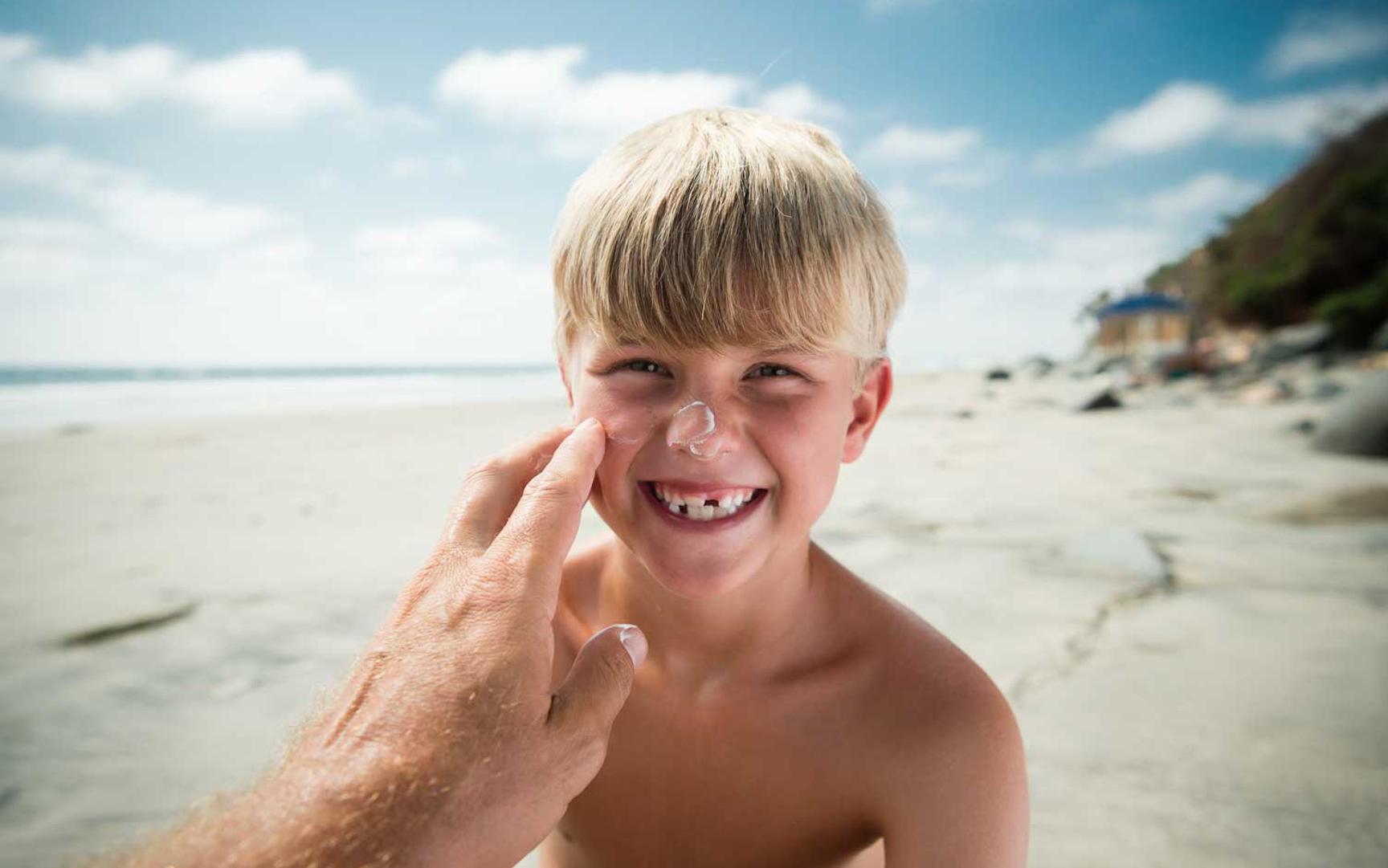 En gutt på stranden har litt solkrem på nesen