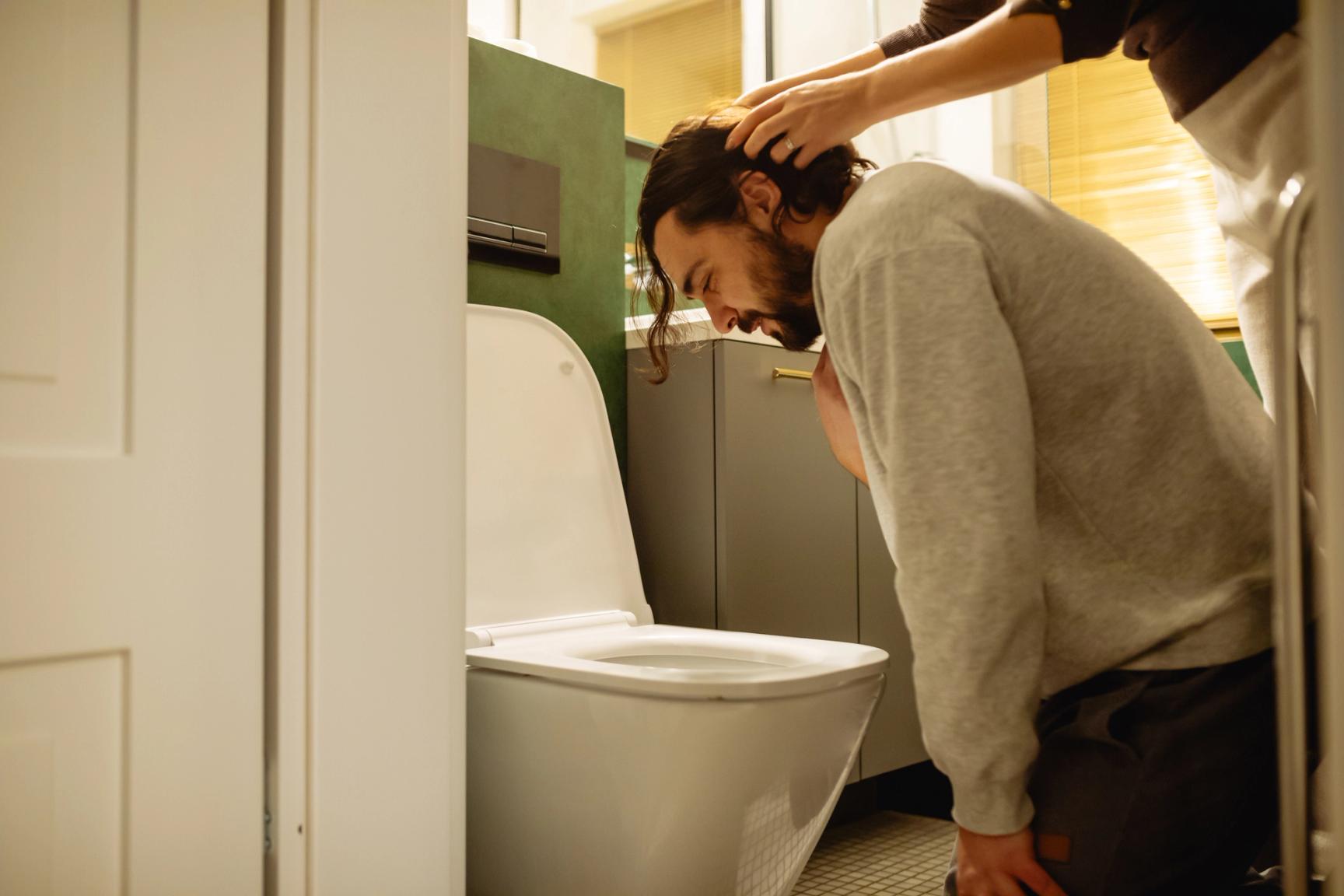 Mann sitter lent over toalettet og holder seg til halsen