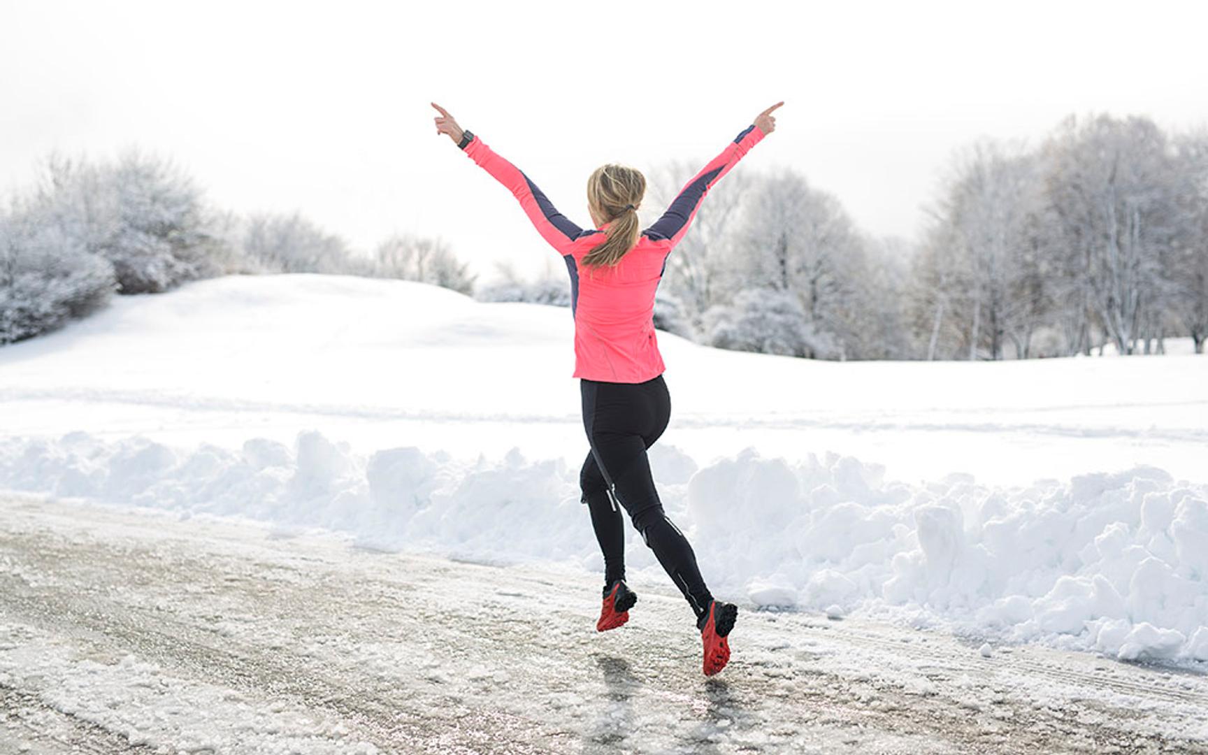 Kvinne som jogger med hendende opp i været av glede på glatt føre i snølandskap.