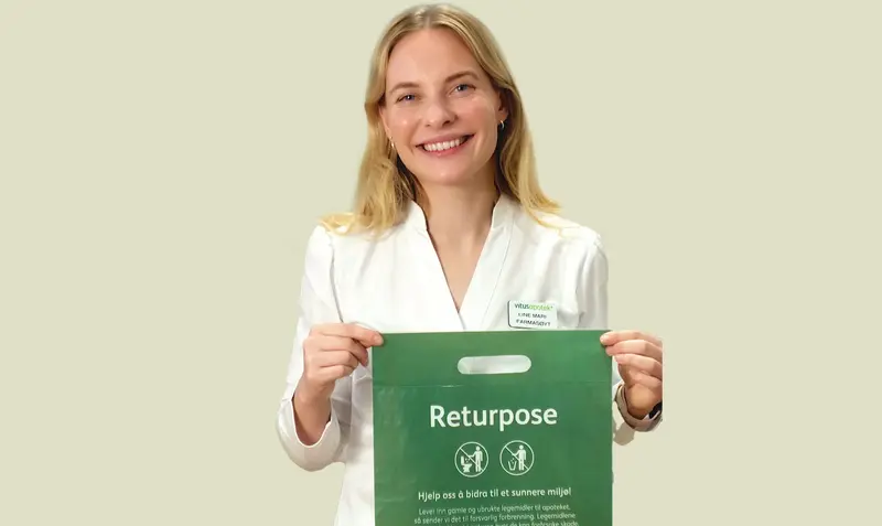 Farmasøyt i hvit uniform holder opp en grønn returpose for retur av medisiner