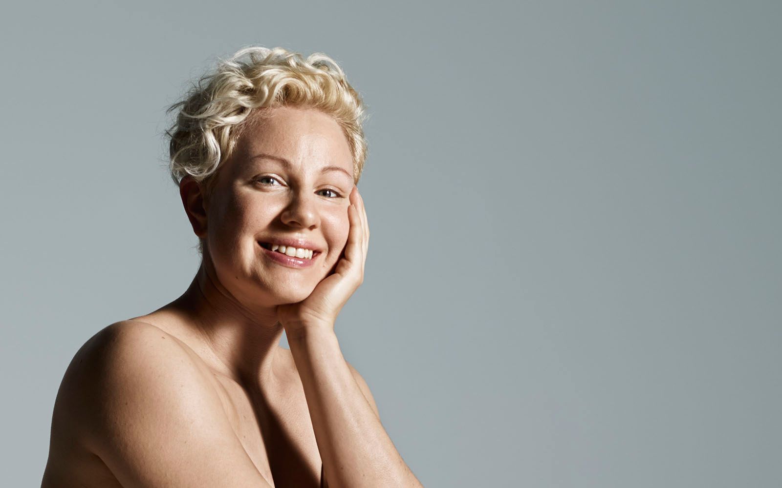 Dame som smiler til kamera og holder den ene hånden mot kinnet