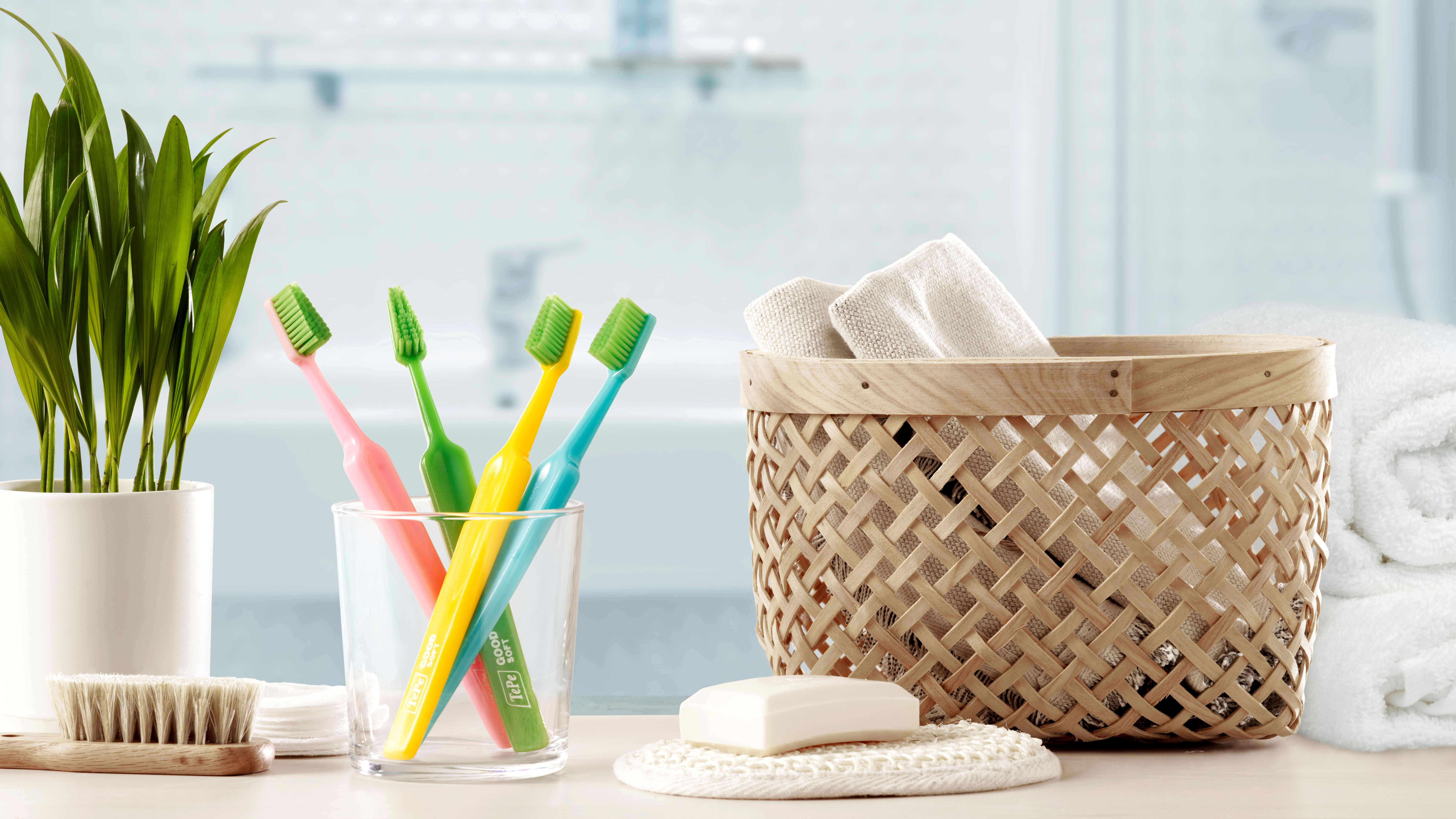 Bilde av en grønn plante, et glass med fire tannbørster, en kurv med håndkler og en såpe