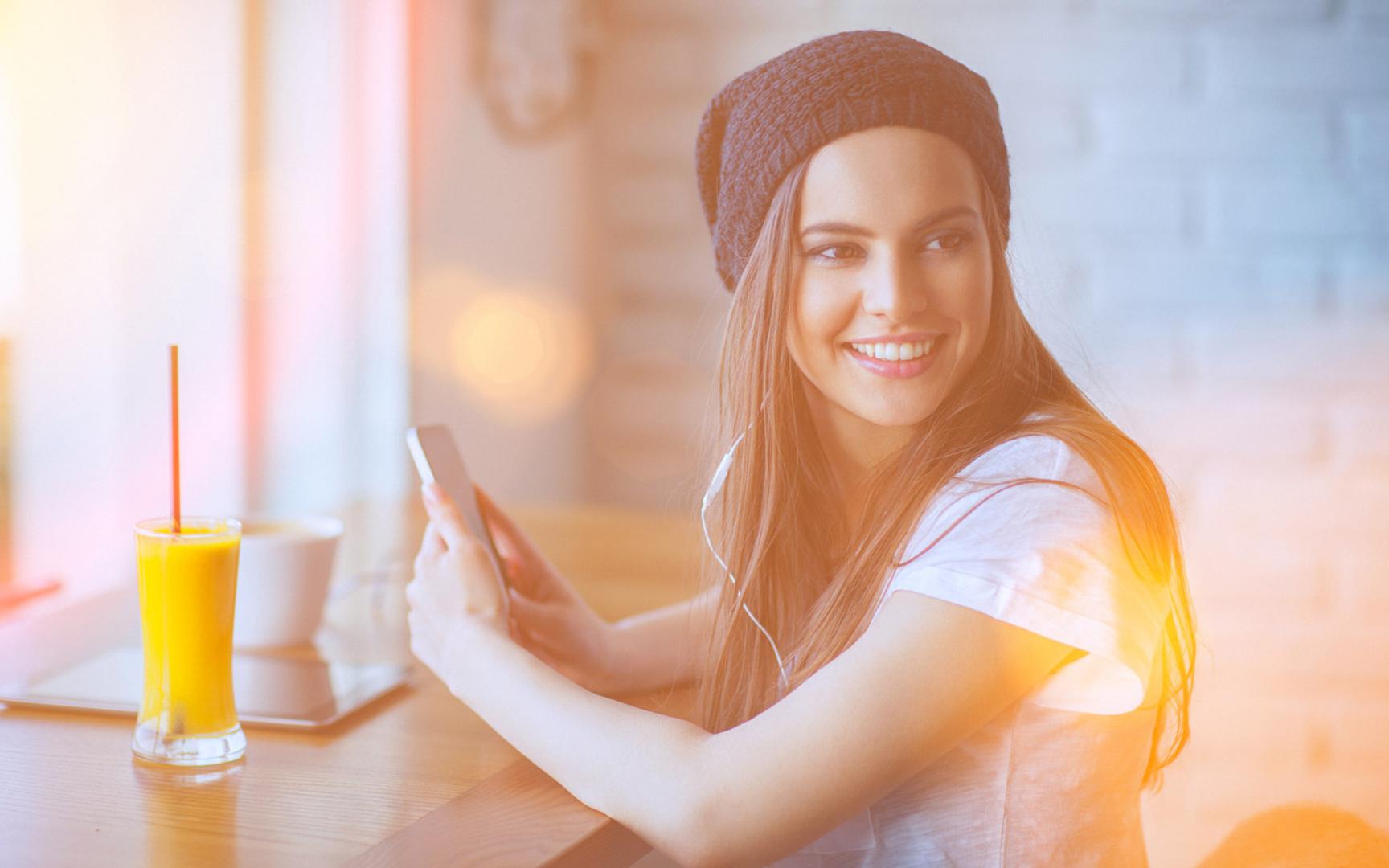 Bilde av en ung dame som smiler og holder en mobiltelefon.