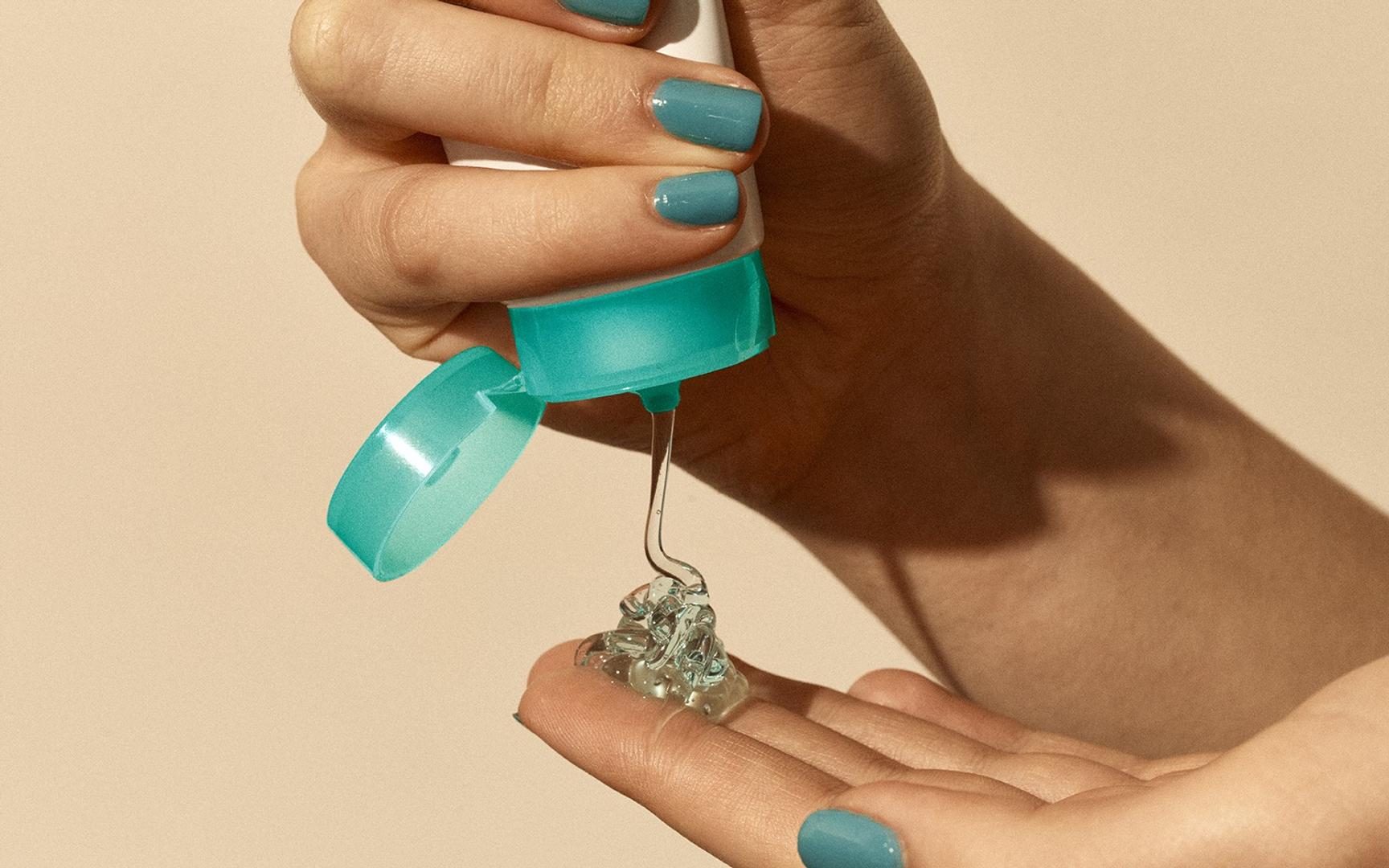 To hender med turkis negle lakk spruter gele fra en tube