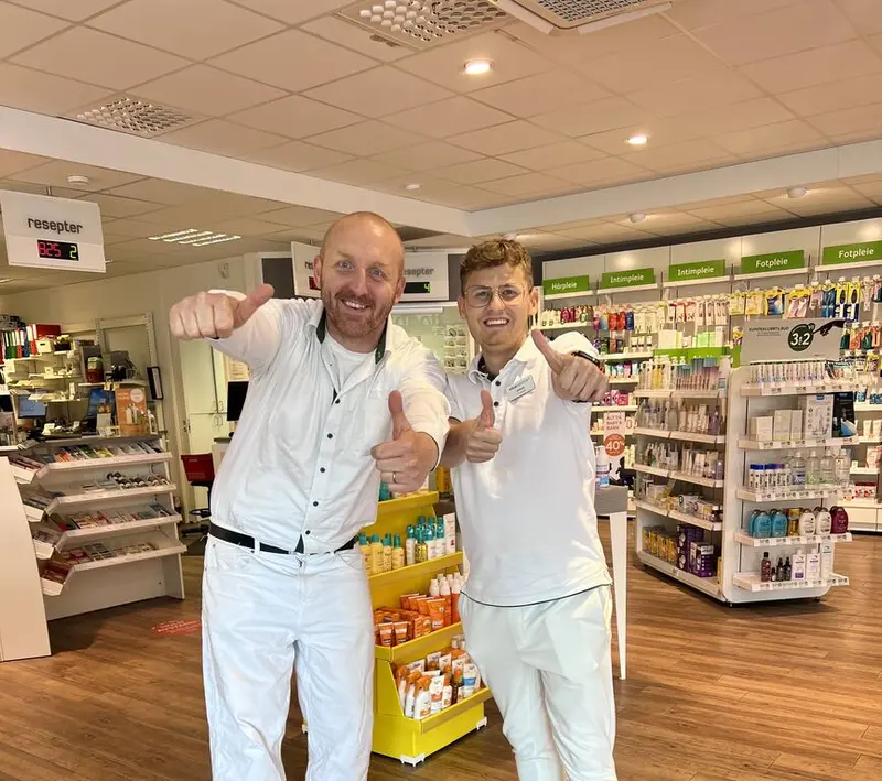 Bilde av Jakub og en kollaga i uniform som smiler og holder to tomler opp i været inne på et apotek