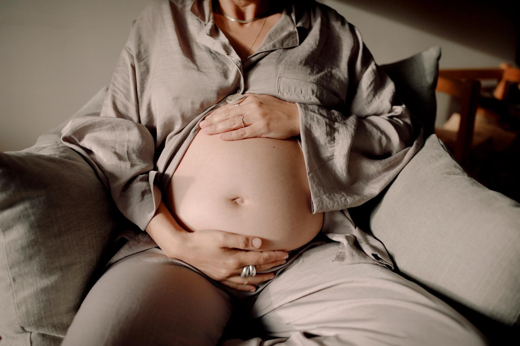 Gravid kvinne sitter i sofa og holder en hånd på magen