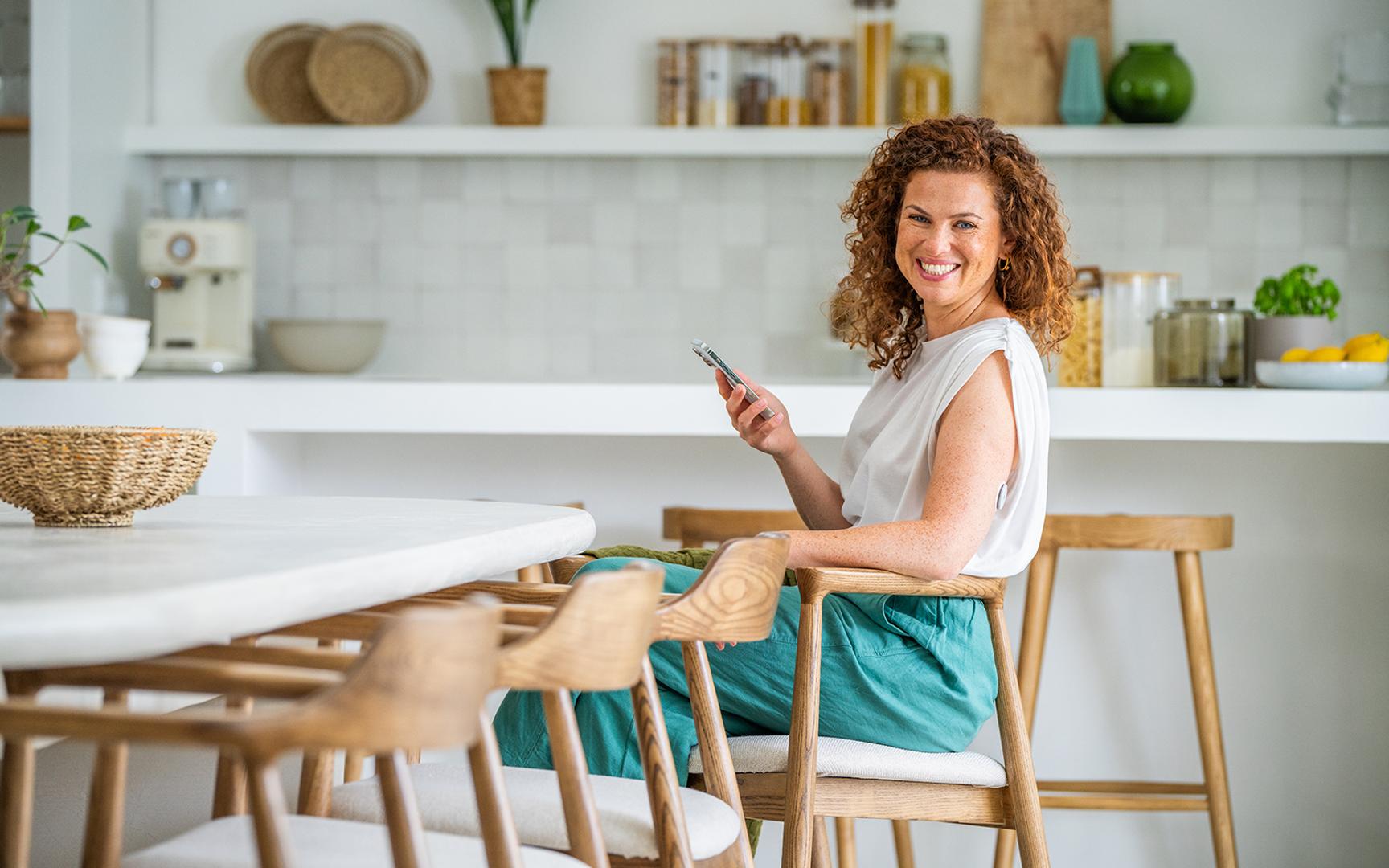 Kvinne med CGM sensor i overarmen og mobiltelefon i den ene hånden