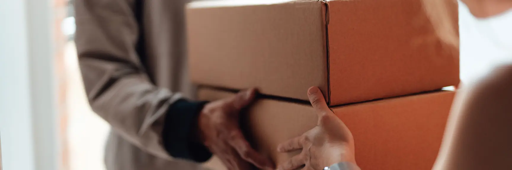 En dame får levert to store pakkesker i hendene i en døråpning