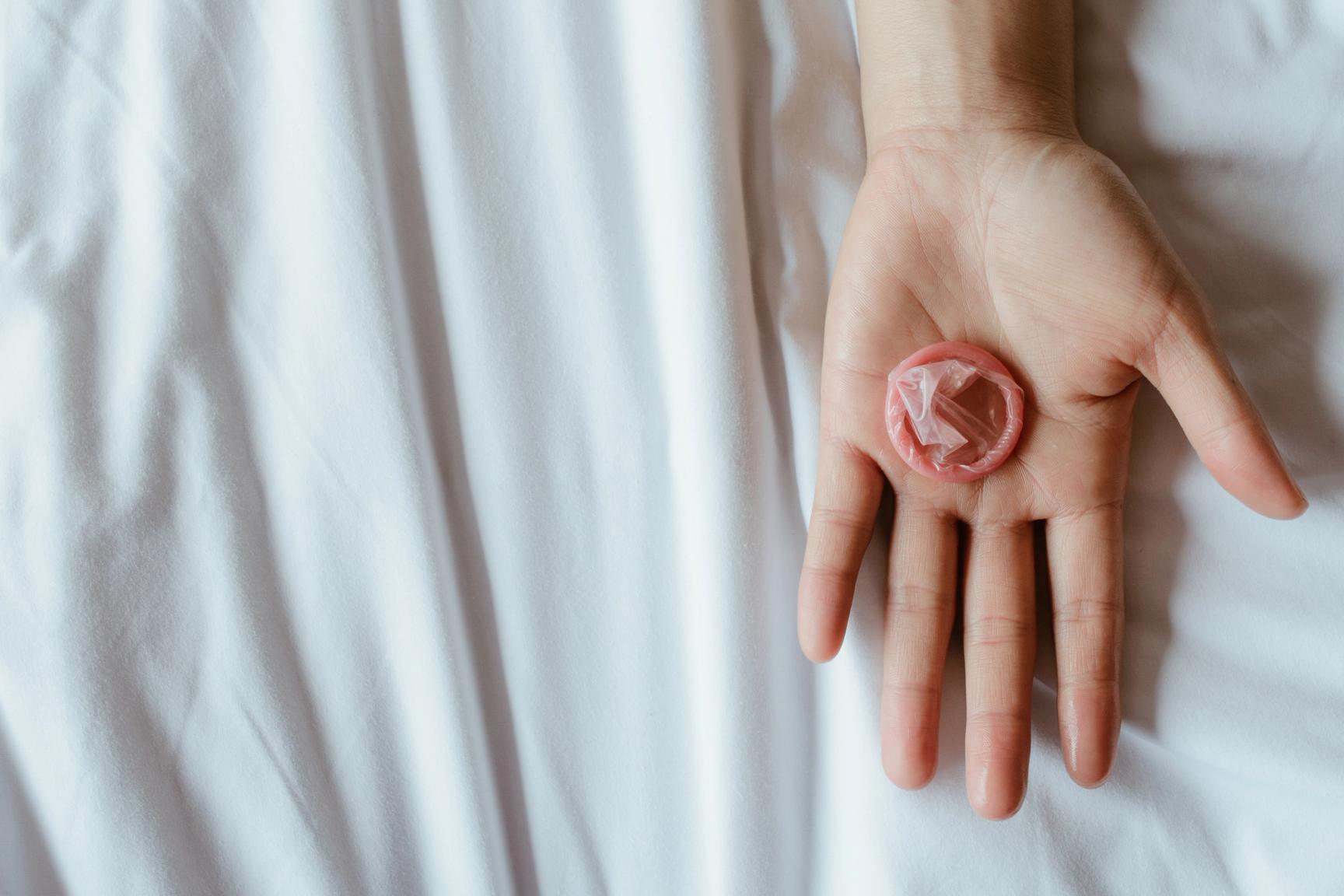 En hånd ligger over et hvit laken med en rød kondom