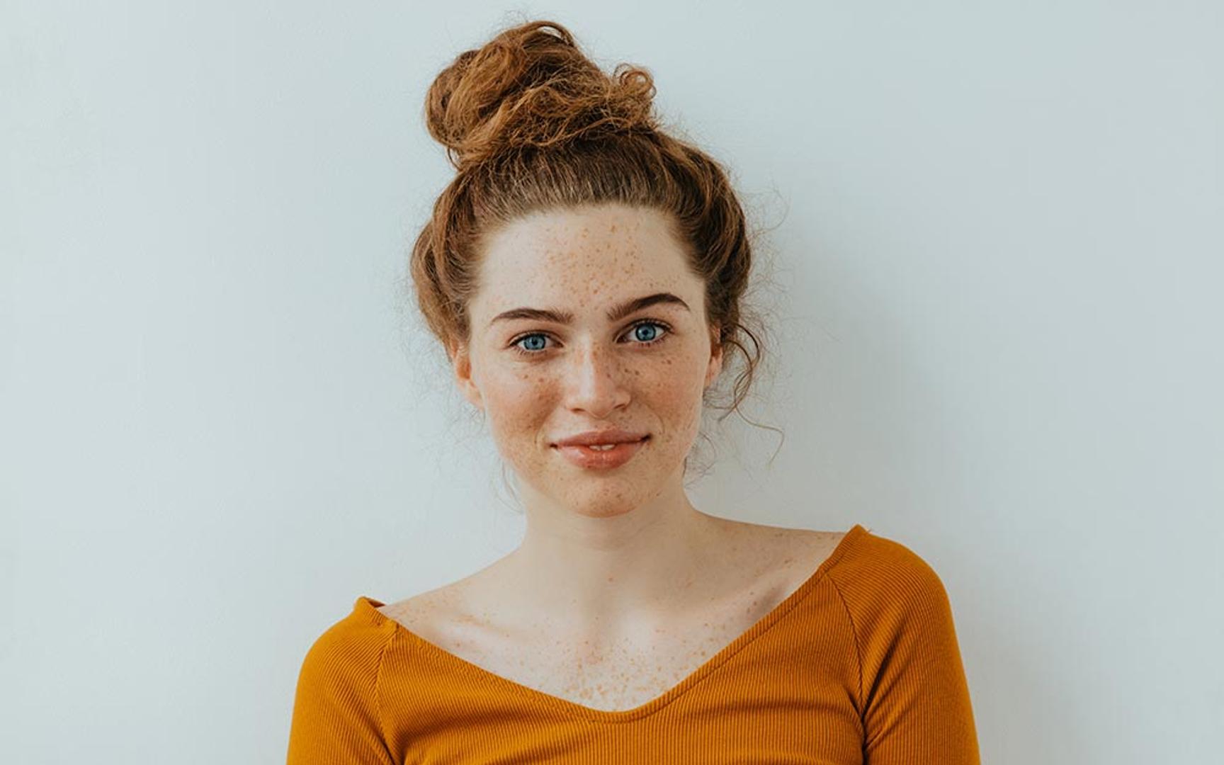 En dame med håret satt opp og orange genser som ser mot kamera