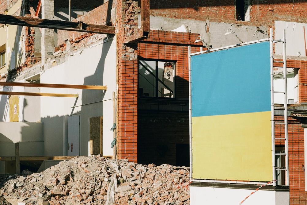 Photo of Ukrainian flag with a demolished building in the background.
