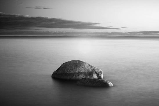 Black and white, infrared, slow exposure time photo of a rock in sea.