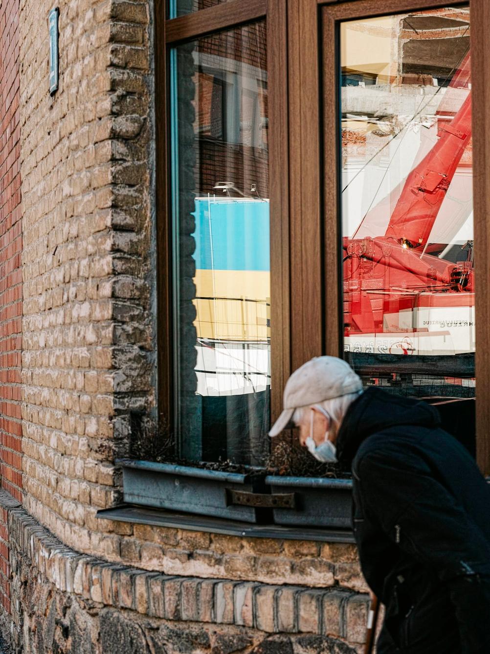 Photo of an old lady walking across a window containing reflection of an Ukrainian flag.