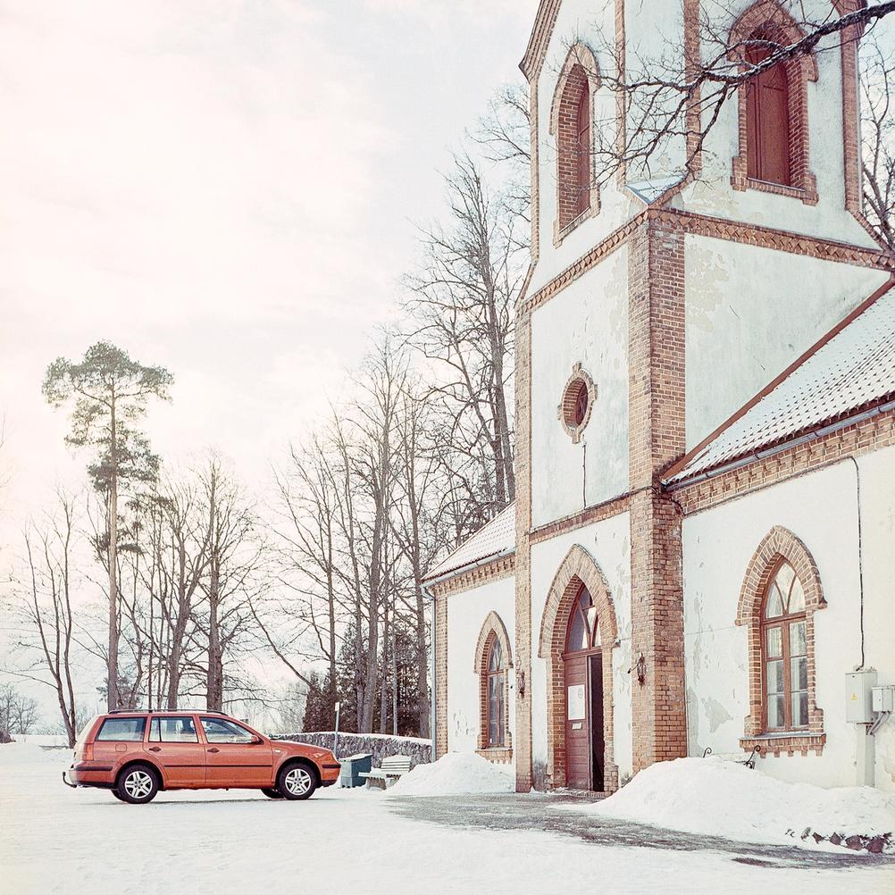 Photo of a red car next to a church.