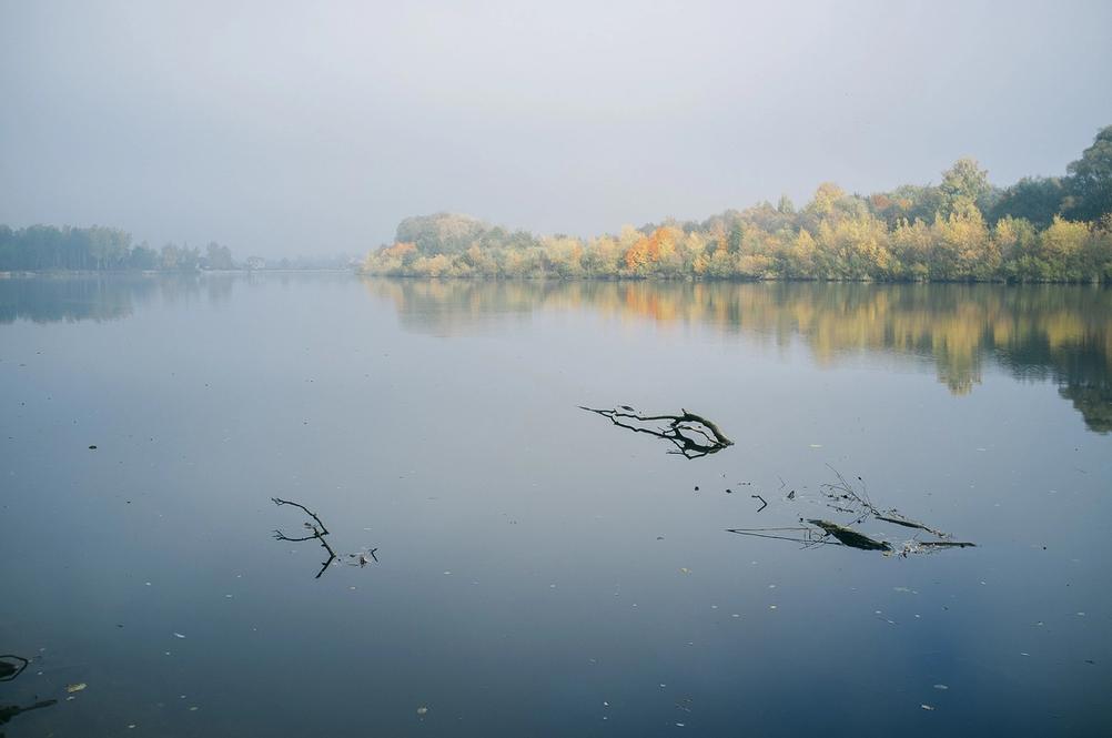 Photo of a river in slight mist with autumn trees in the distance.