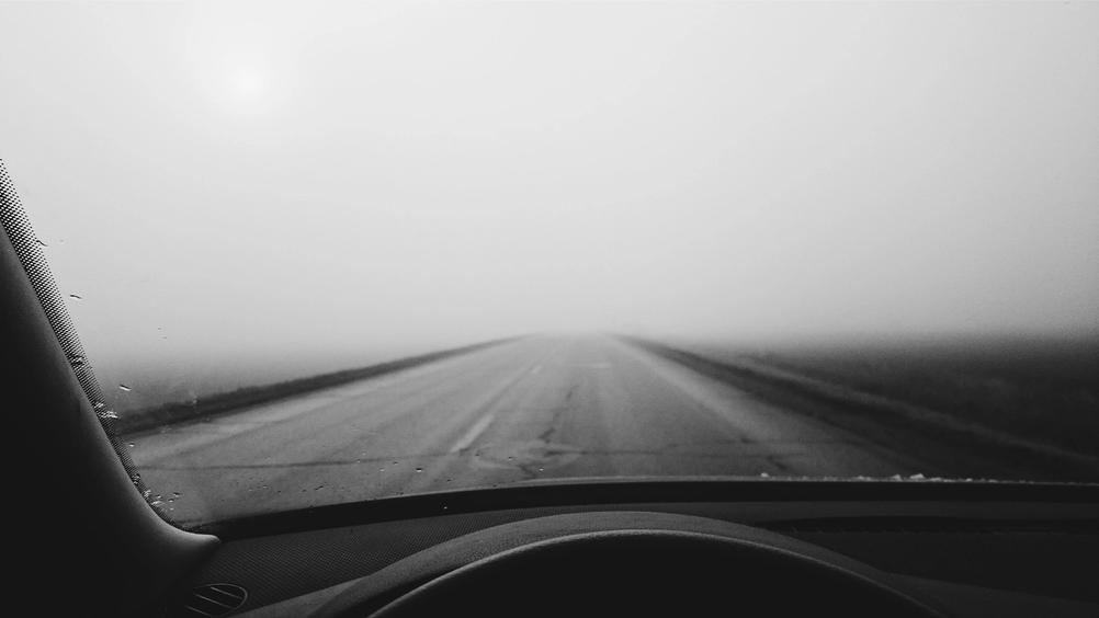 Photo shot through car windshield of a road in mist.