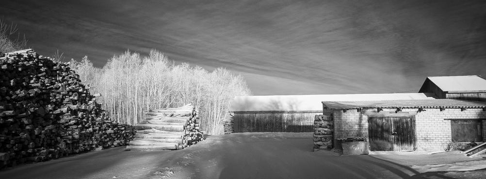 Black and white infrared photo of a wintery scene with some snow and woods.