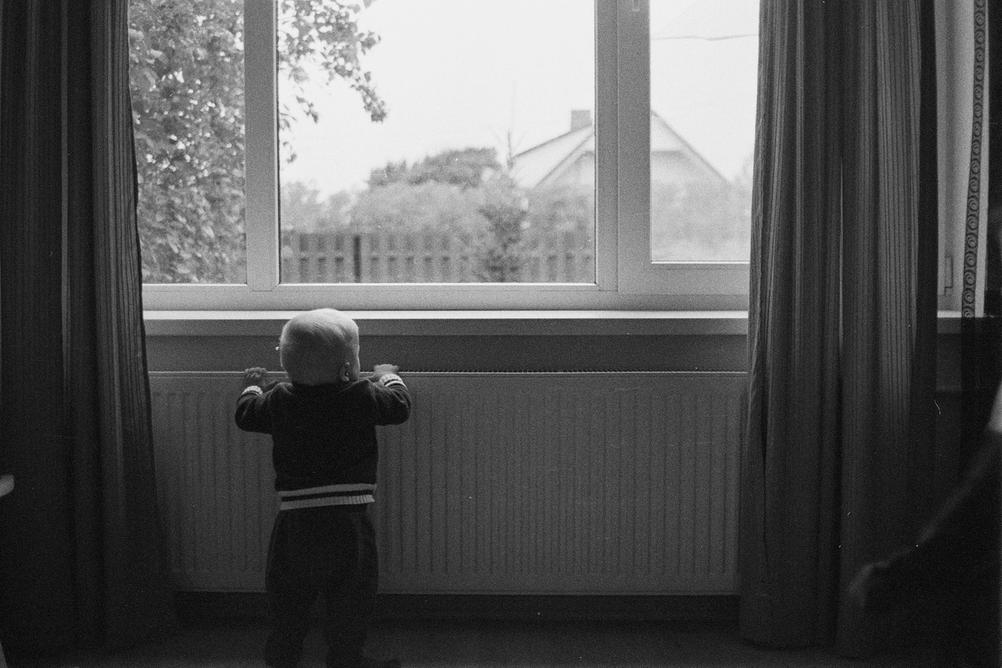 Small boy trying to look outside window.