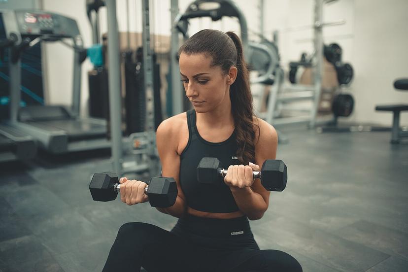 Phụ nữ ngồi trên sàn phòng tập, tập tạ tay đơn cho người mới bắt đầu