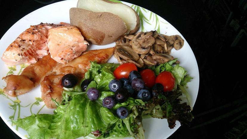 Bữa ăn cân đối có cá hồi, salad, khoai tây, cà chua và quả mọng, minh hoạ ăn uống lành mạnh