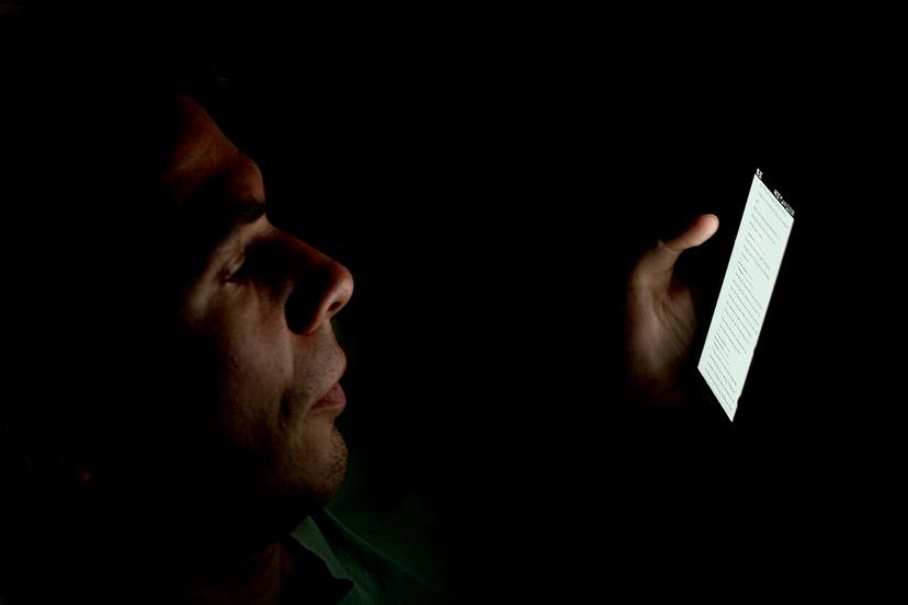 Người dùng điện thoại trước khi ngủ trong phòng tối, mặt sáng lên vì màn hình
