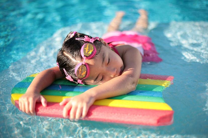 Cô gái nghỉ giữa buổi tập bơi, tay bám phao xốp trong hồ bơi