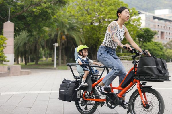 Parent riding an orange Tern Quick Haul through a city square with a child in the rear seat