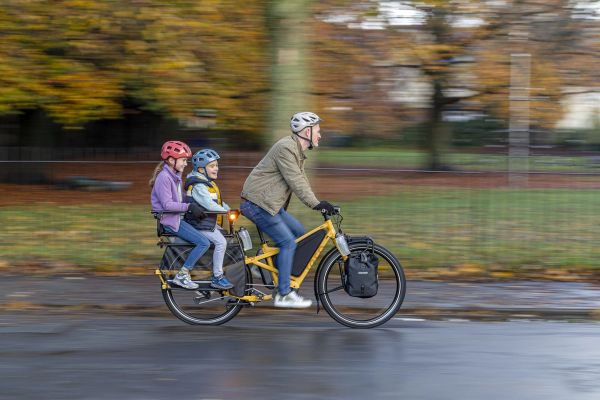 Parent riding a Tern Orox through autumn leaves with two kids on the back