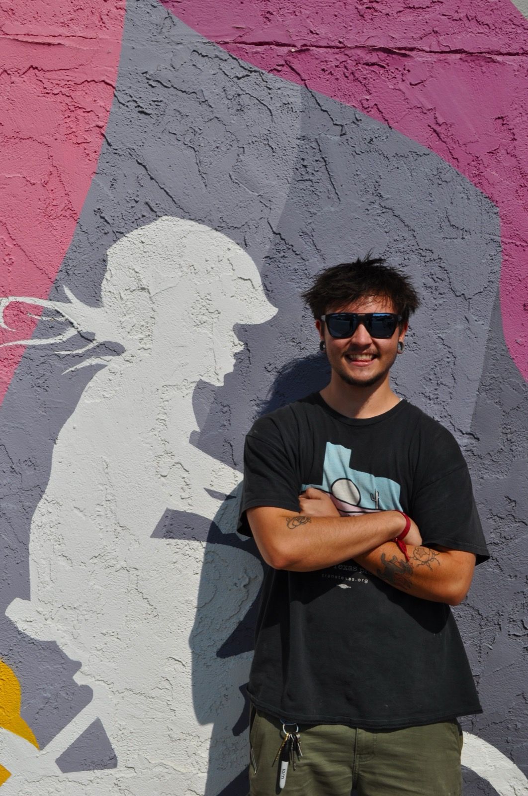 Noah smiling with arms crossed in front of the Hardt Family Cyclery mural