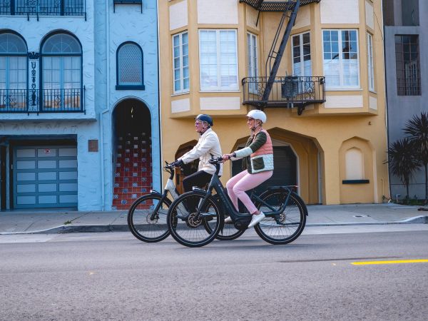 Two riders on Gazelle Avignon e-bikes passing colorful city houses