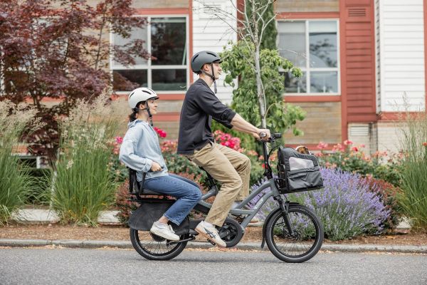 Parent riding a Tern HSD past a house with a child riding on the back