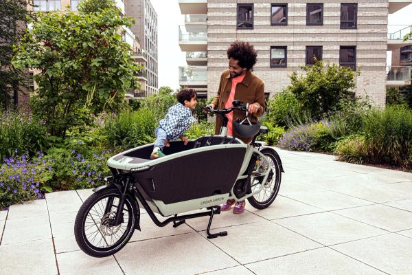 Urban Arrow FamilyNext Pro in a courtyard, parent holding the bars while one child climbs into the cargo box
