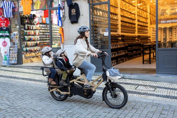 Parent riding a Tern GSD past a shopfront with two kids in the Clubhouse seats