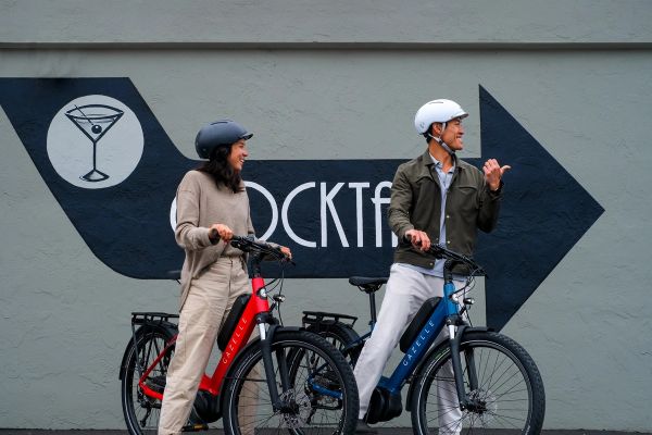 Two riders with Gazelle Medeo e-bikes chatting by a painted wall sign
