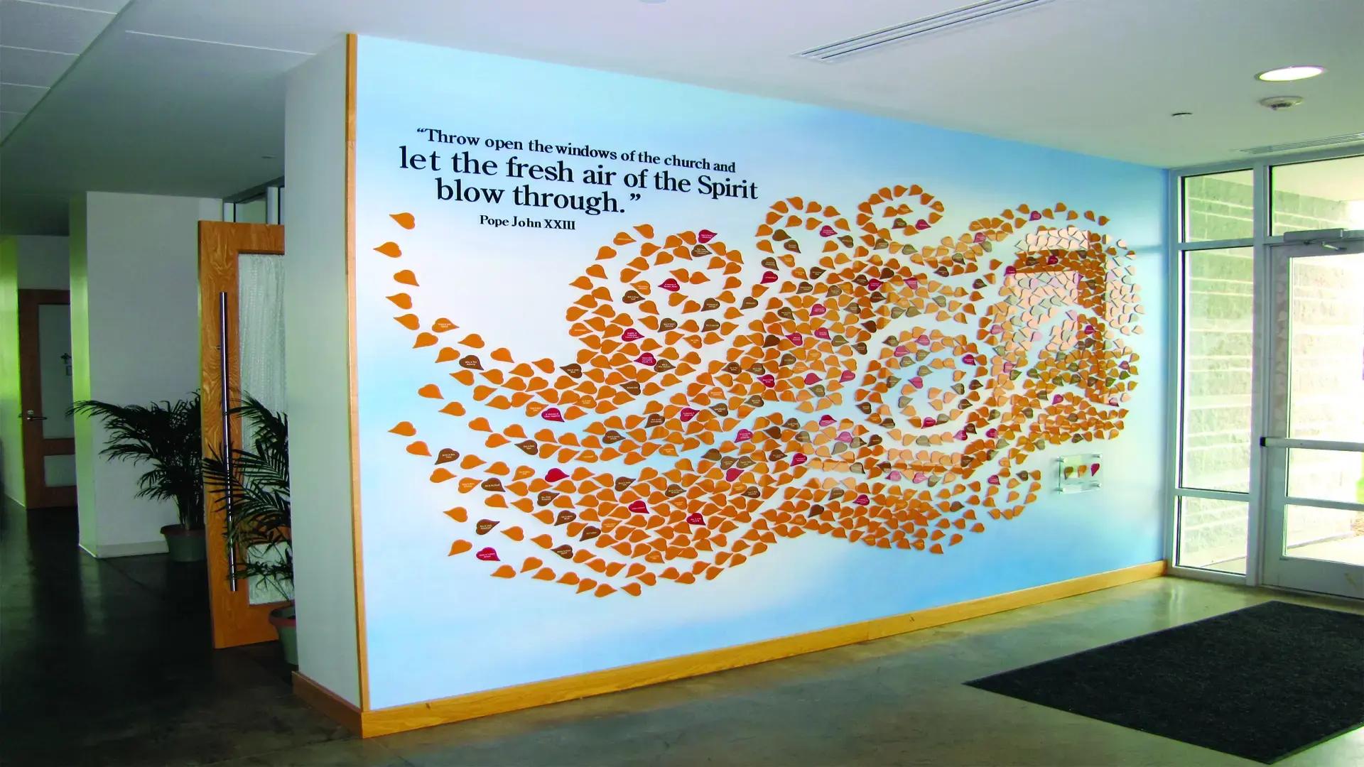 Leaf donor recognition wall at St. John’s Church with updateable leaves blowing across the wall, symbolizing generosity, faith, and lasting impact.