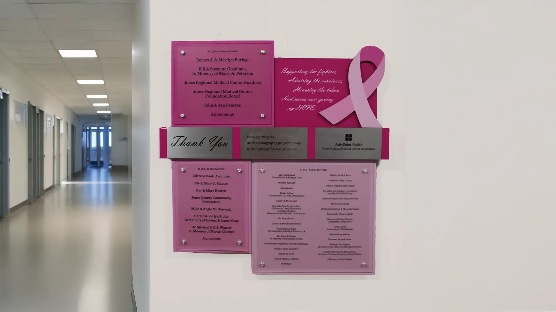Pink donor recognition wall with layered acrylic panels, printed donor names, and a dimensional breast cancer awareness ribbon.