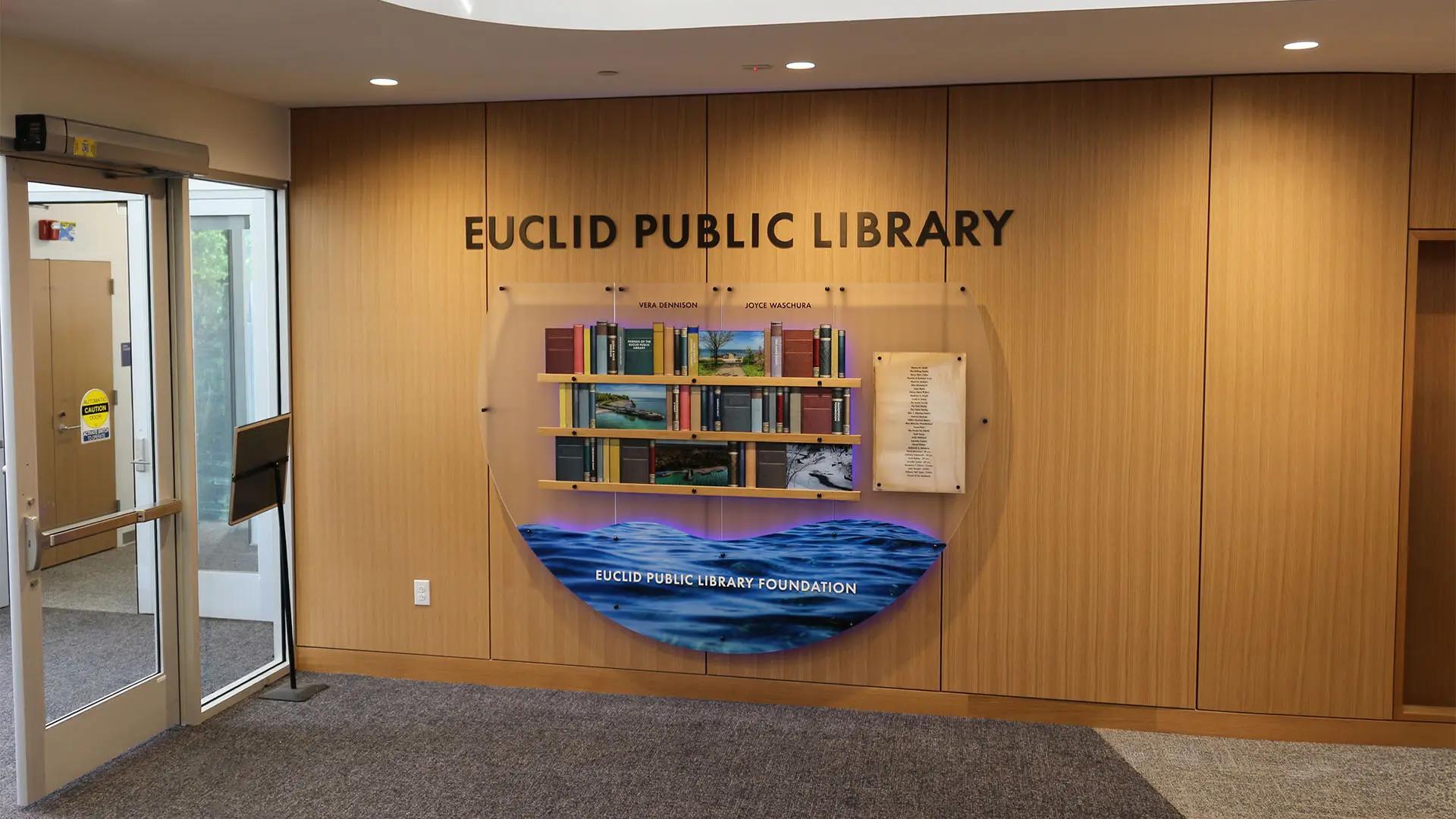 Custom donor recognition wall at Euclid Library with dimensional lettering, integrated donor books and plaques, LED-lit water graphic centerpiece.