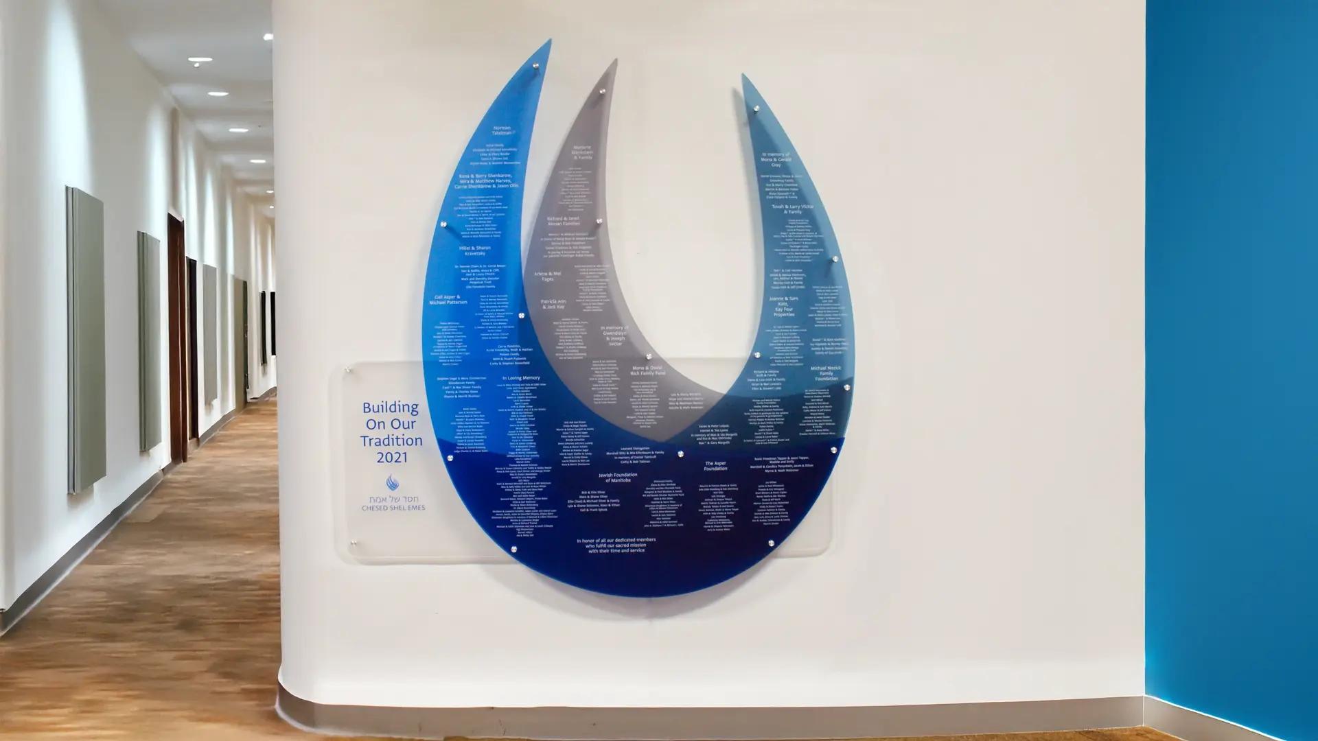 Custom donor recognition wall with layered acrylic flame design and printed donor names displayed in a Jewish synagogue corridor.